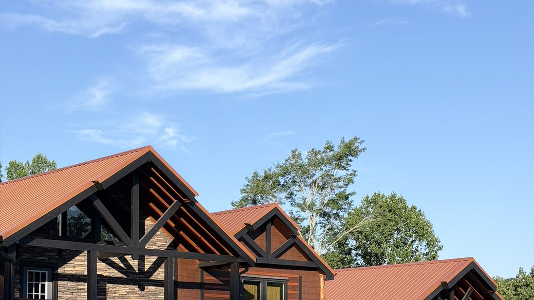 Completed cabin in Sevier County, Tennessee — timber-frame gable with exposed trusses, stained board-and-batten siding, and a standing-seam metal roof.