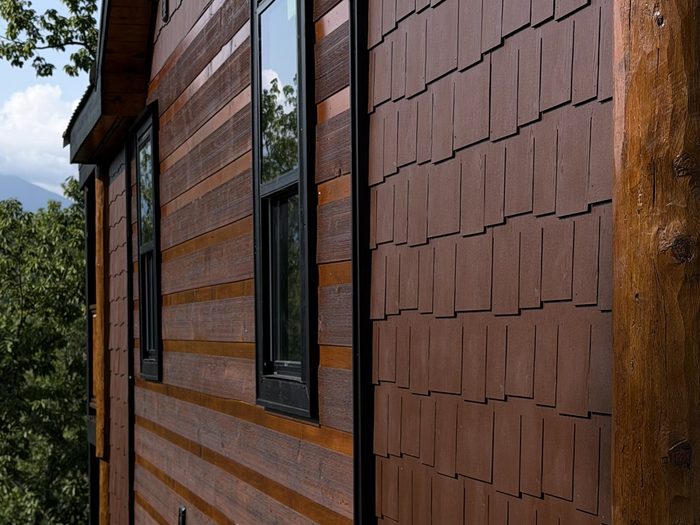 Stained board-and-batten and shake siding on a completed cabin exterior in raking afternoon light.